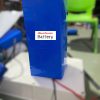 A Lithium ion battery pack in the making with dark blue heatshrink cover, electrical cords black and red connected.