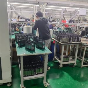 a battery assembly station with a man standing next to a table of li-ion battery packs in the making.